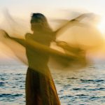 person moving/dancing in-front of the ocean during sunset