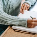 person writing in a notebook whilst sitting at a desk
