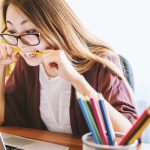 person looking at a computer whilst biting a pencil