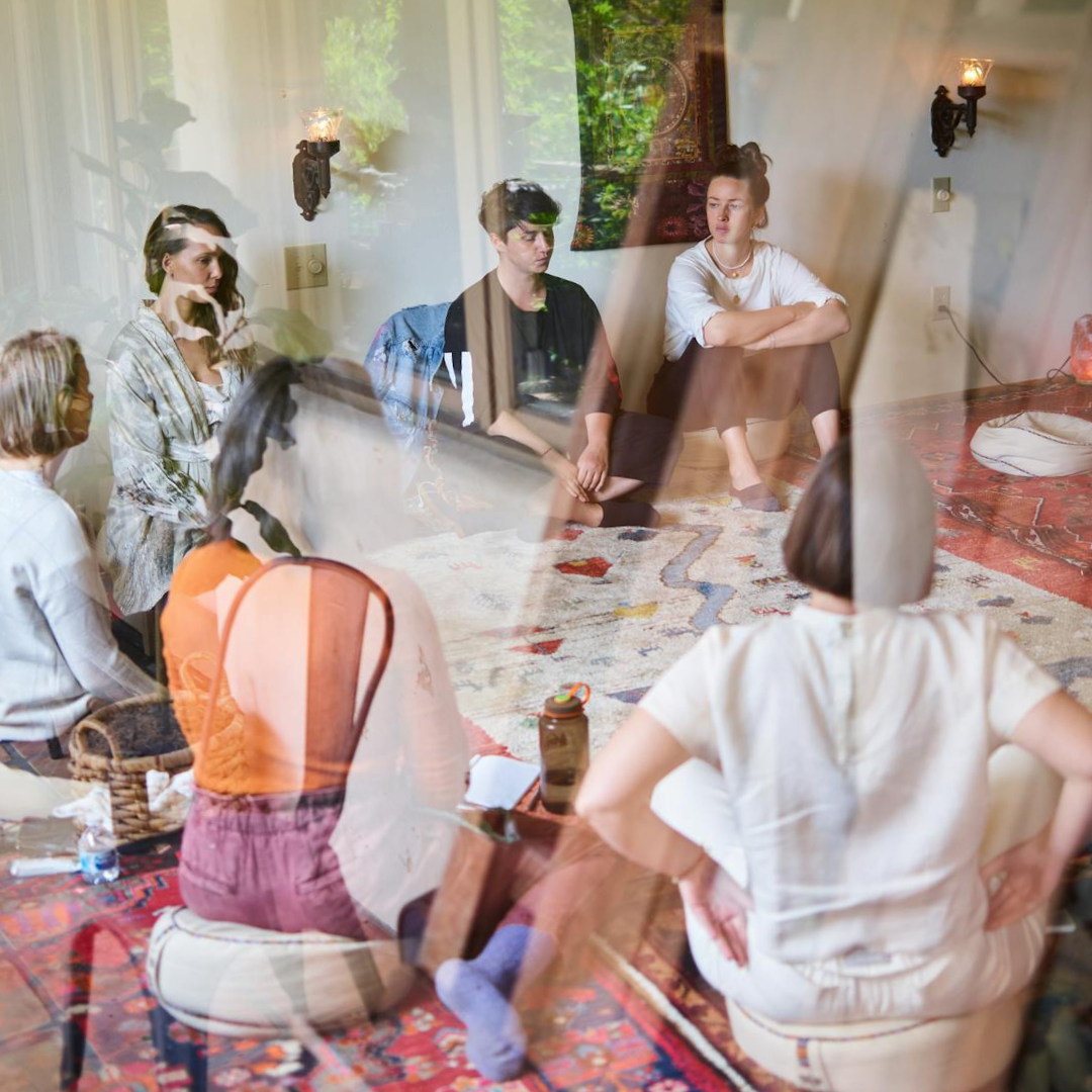 Double-exposure photograph of a group of people sitting together on the floor or a large room.