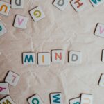 Photo consists of a cream colored, wrinkled fabric background with scattered, colorful letter tiles in a square shape that have been arranged to spell out the word "mind."